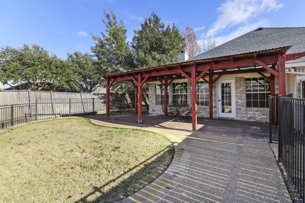 A backyard with a wooden deck and pergola next to a grassy lawn and trees.