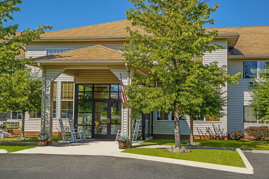 A suburban building entrance with a porch and rocking chairs, surrounded by greenery.