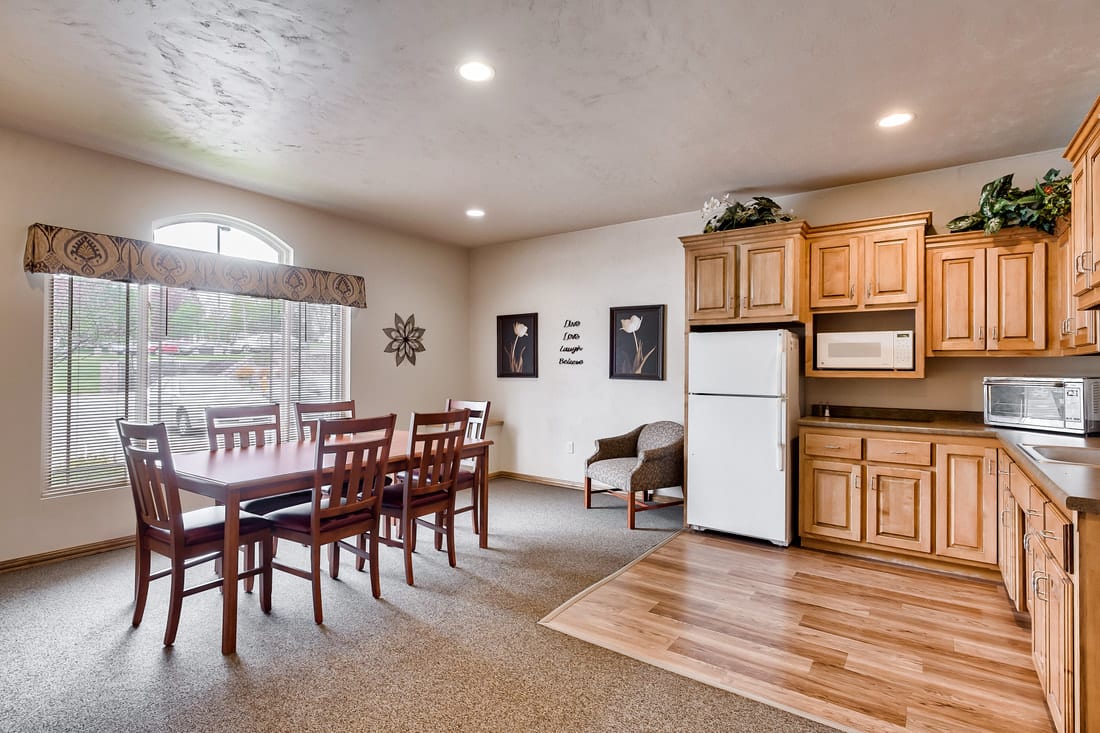 A well-lit dining area with a wooden table and chairs adjacent to a compact kitchen featuring a refrigerator and microwave.