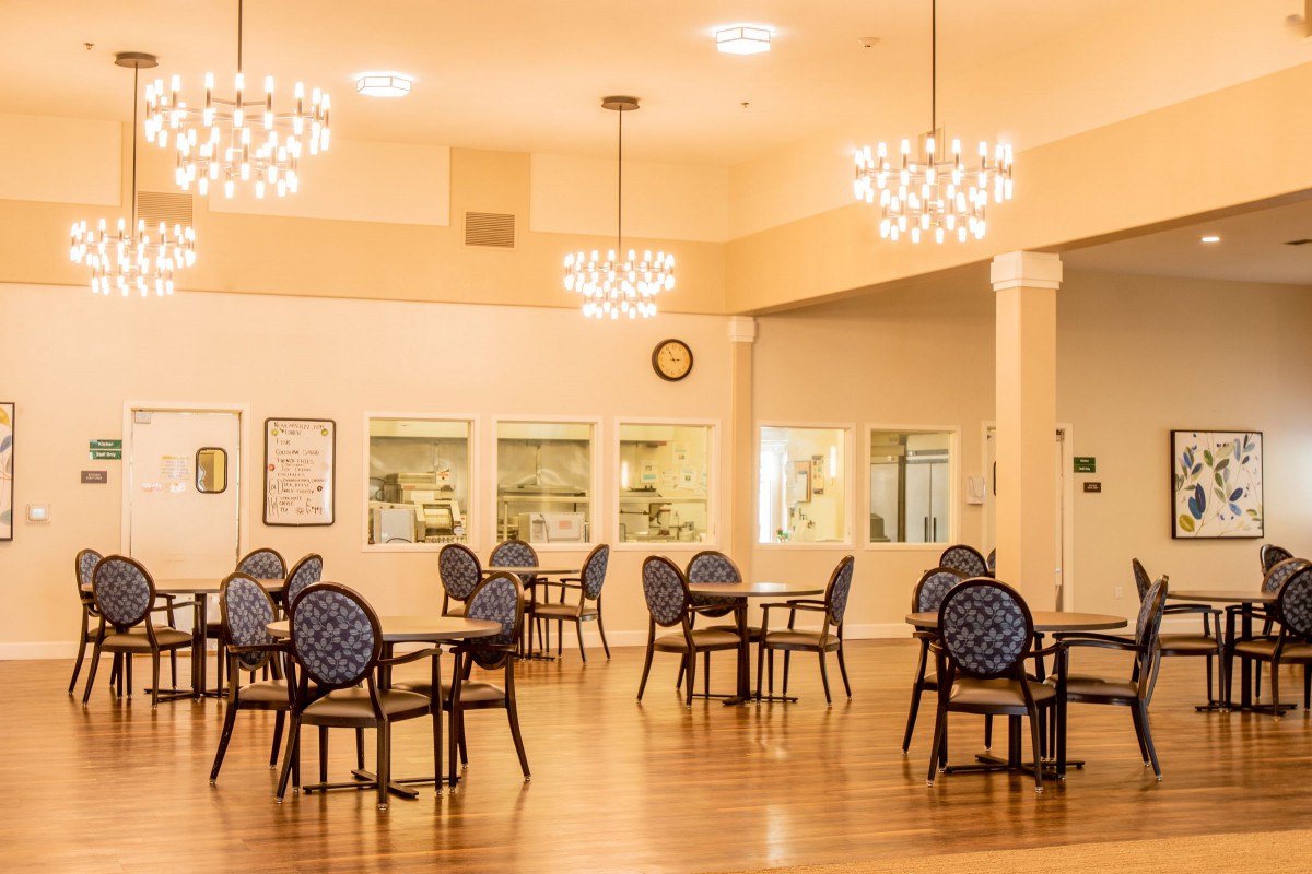 An elegant dining area with multiple tables and chairs, illuminated by chandeliers.