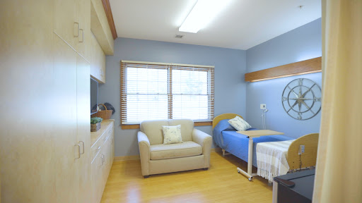 A well-lit hospital patient room featuring a bed, a sofa, and natural light from the windows.