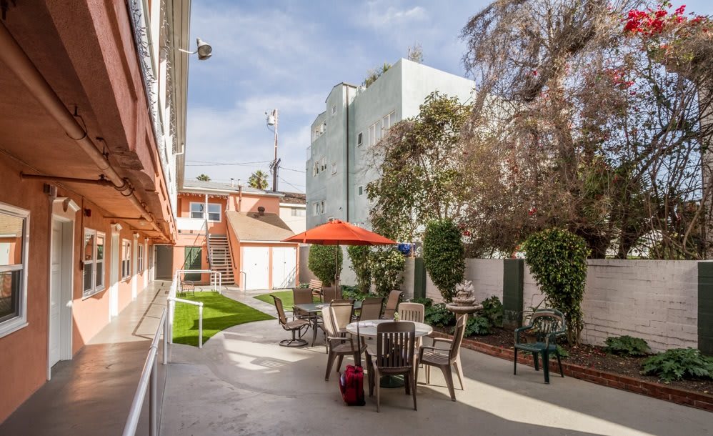 An outdoor patio area with tables, chairs, and umbrellas in an urban setting surrounded by buildings and trees.