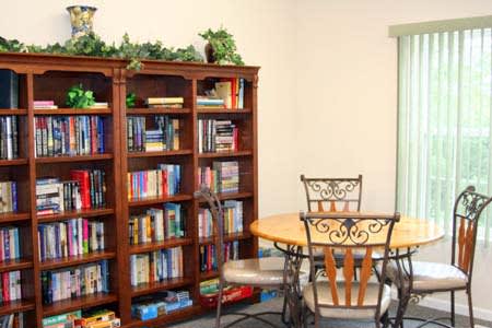 A cozy library room featuring a wooden bookshelf filled with books and a round table with chairs.