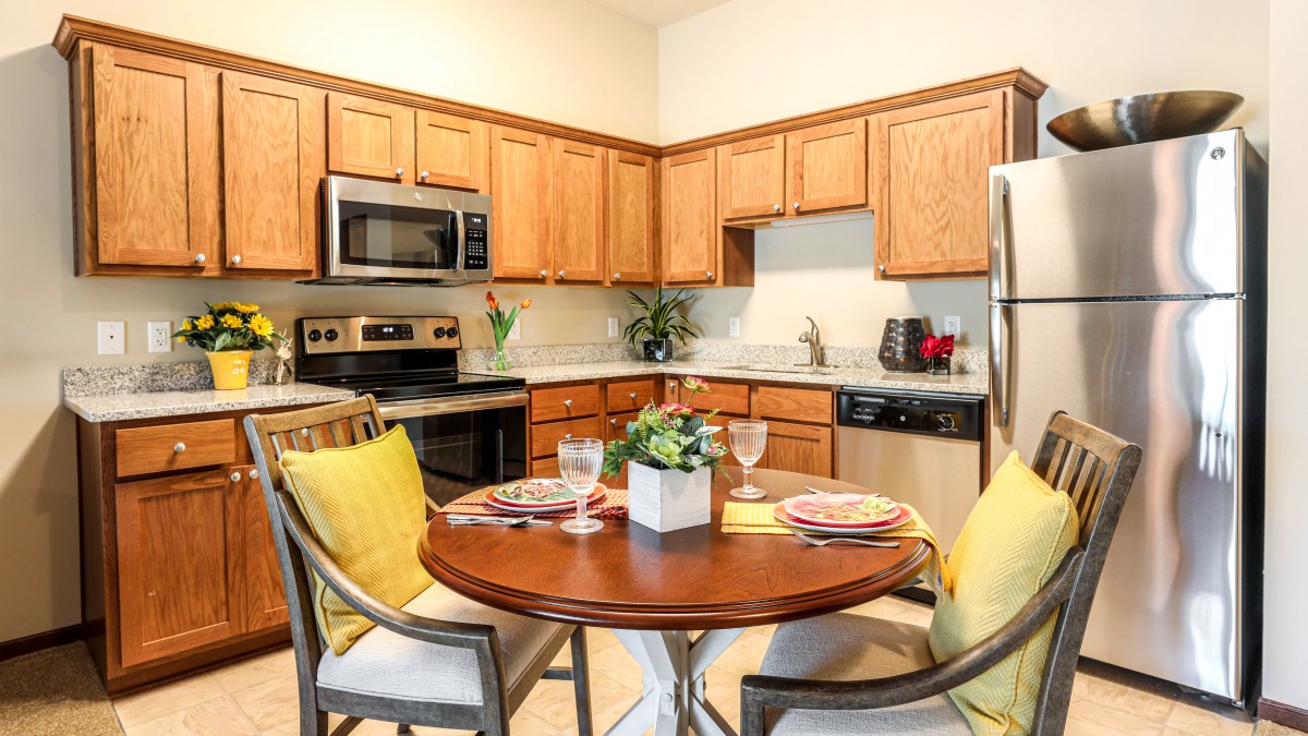 A modern kitchen with wooden cabinets, stainless steel appliances, and a cozy dining area featuring a round table with yellow-accented decor.