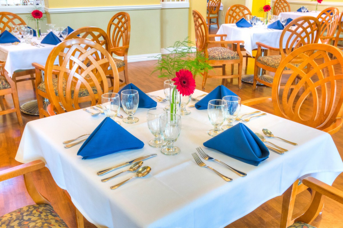 A well-set dining table in a restaurant with blue napkins and a floral centerpiece.