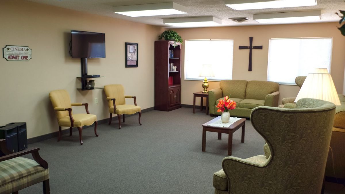 A cozy waiting room with comfortable seating, a television, and decor including a cross on the wall.