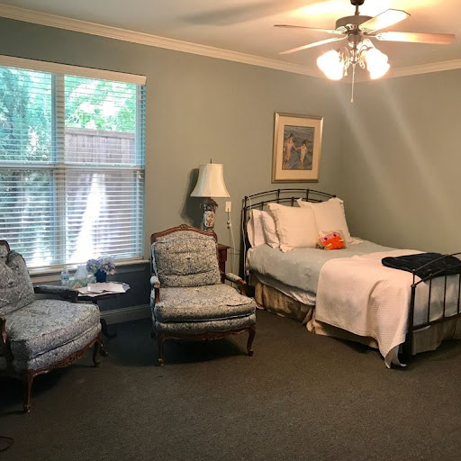 A cozy and well-lit bedroom featuring a single bed, armchairs, and natural light from the window.