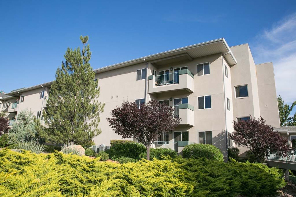 A modern apartment building with balconies, surrounded by well-maintained landscaping and a clear blue sky.