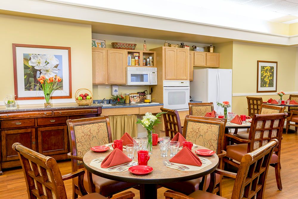 A cozy dining area with a round table set with red napkins and surrounded by wooden chairs, adjacent to a modern kitchen.