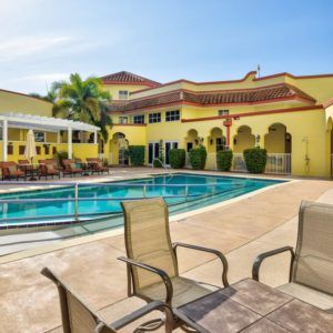 An inviting outdoor pool area with chairs and a sunny building in the background.