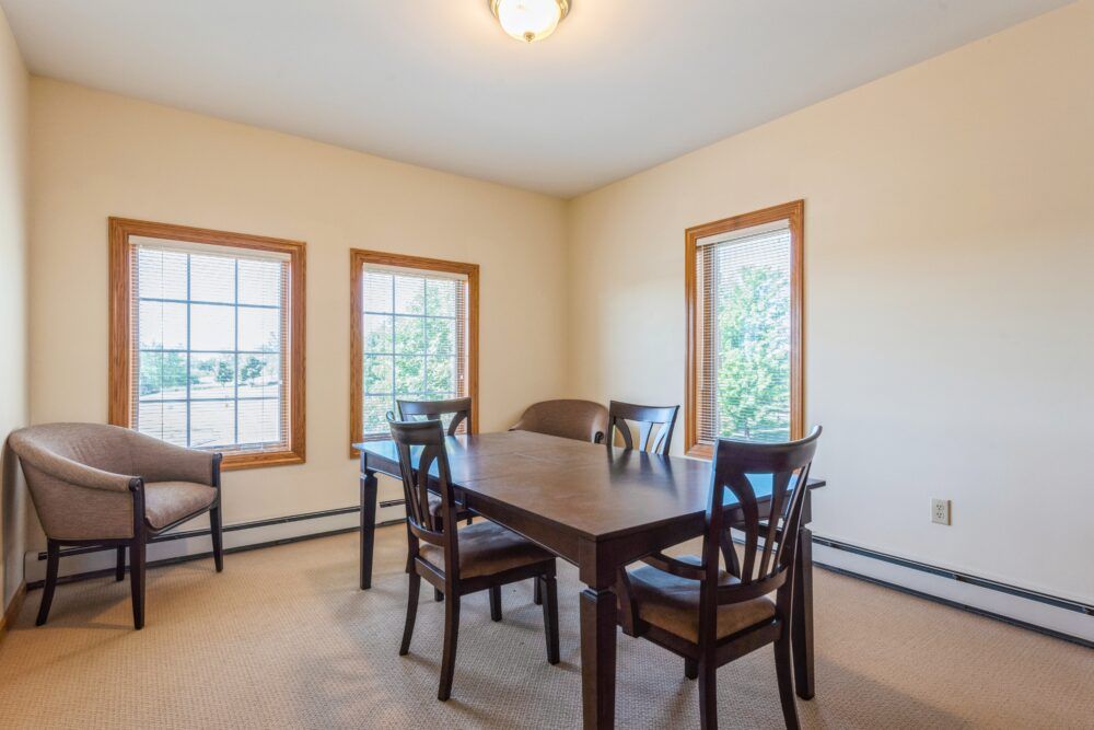 A cozy dining room with a wooden table, surrounded by four chairs and natural light coming through the windows.