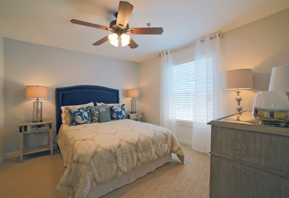 A cozy bedroom with a neatly made bed, ceiling fan, and soft lighting.