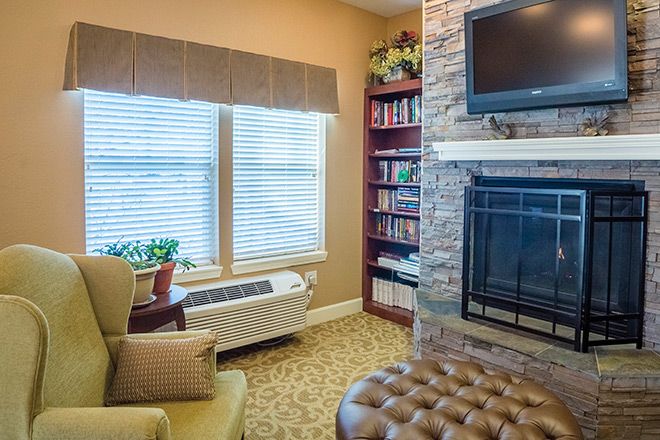 A cozy living room with a fireplace, television, bookshelf, and armchair by the window.