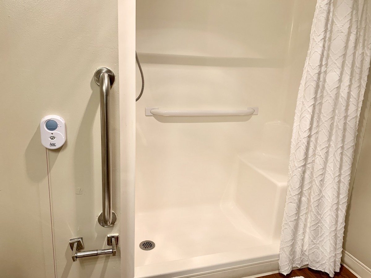 A modern shower with safety features, including a grab bar and a shower curtain.