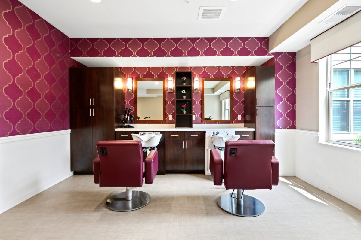 A modern hair salon interior with stylish red chairs and decorative wallpaper.