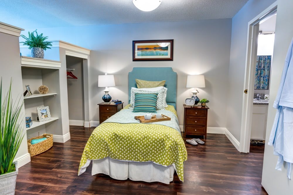 A modern bedroom featuring a single bed with colorful bedding, framed artwork on the wall, and two nightstands with lamps.