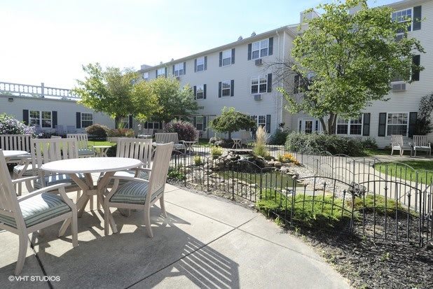 A sunny outdoor patio area with seating and a garden, adjacent to a multi-story building.