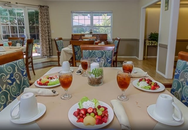 A dining room table set with fruit plates and iced tea, ready for a meal.