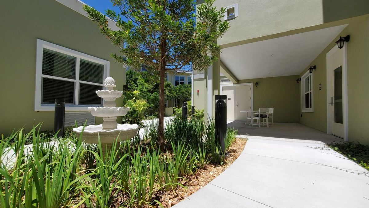 A serene courtyard featuring a central fountain surrounded by lush greenery and a paved walkway.