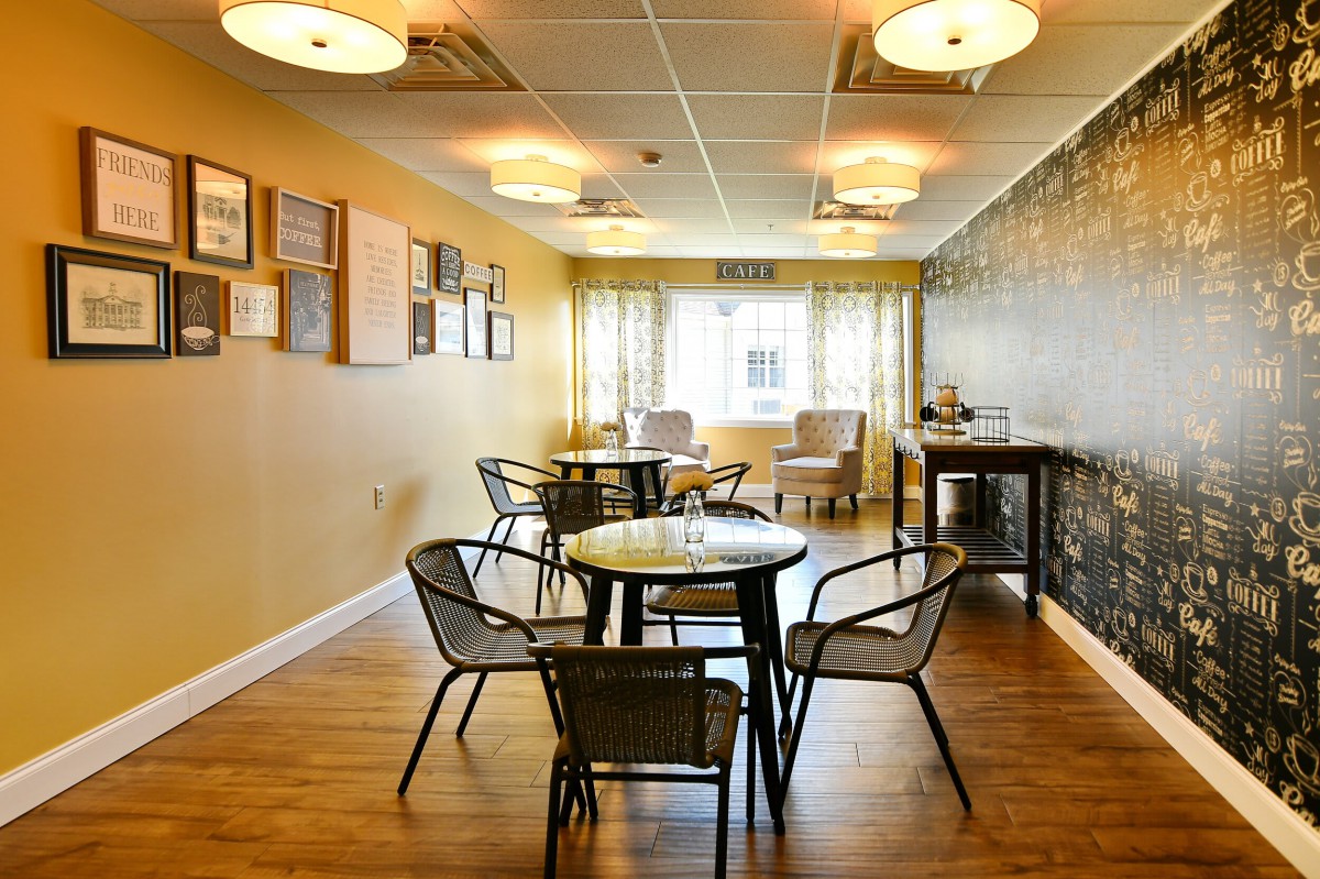 A cozy room with tables and chairs, featuring warm lighting and wooden floors.