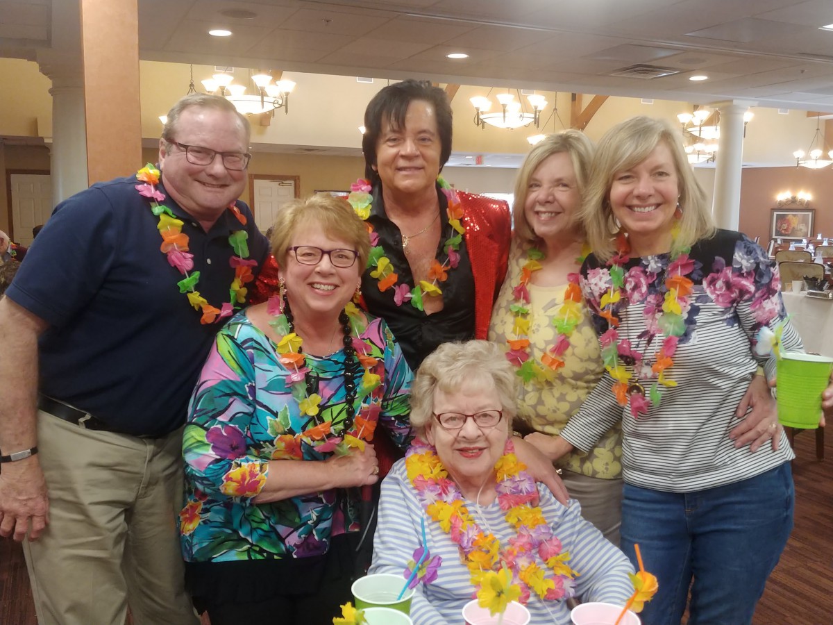 A group of people wearing colorful leis celebrating at a Hawaiian-themed party indoors.