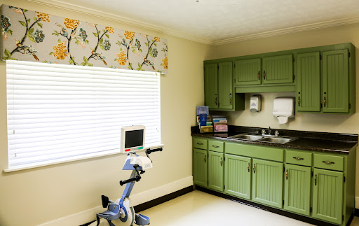 A cozy kitchen featuring green cabinets and a stationary bike, perfect for combining fitness and cooking.