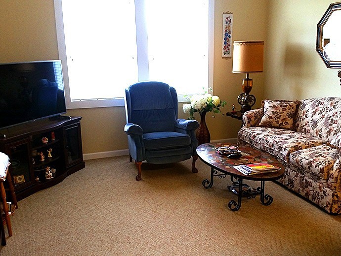 A cozy living room with a blue armchair, floral sofa, and a wooden coffee table.
