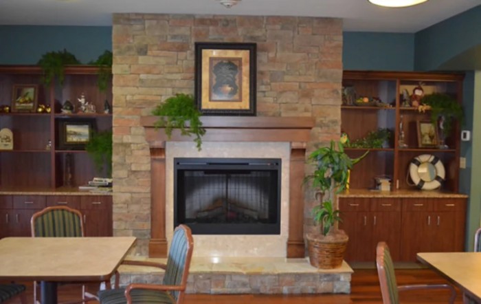 A cozy living room with a brick fireplace, surrounded by plants and wooden furniture.