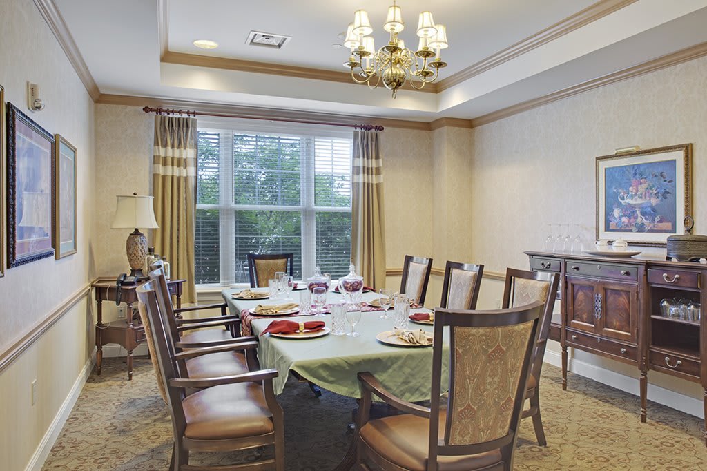 A well-decorated dining room with a large table set for dinner, featuring elegant chairs and a chandelier.