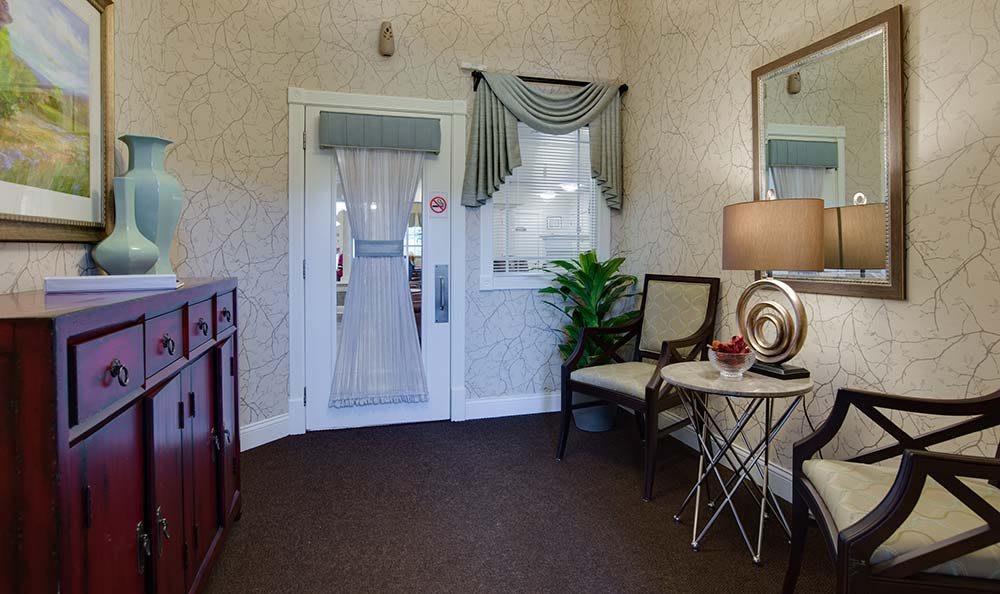 A cozy and elegantly decorated lobby area featuring comfortable chairs, a side table with a lamp, decorative items, and a potted plant.