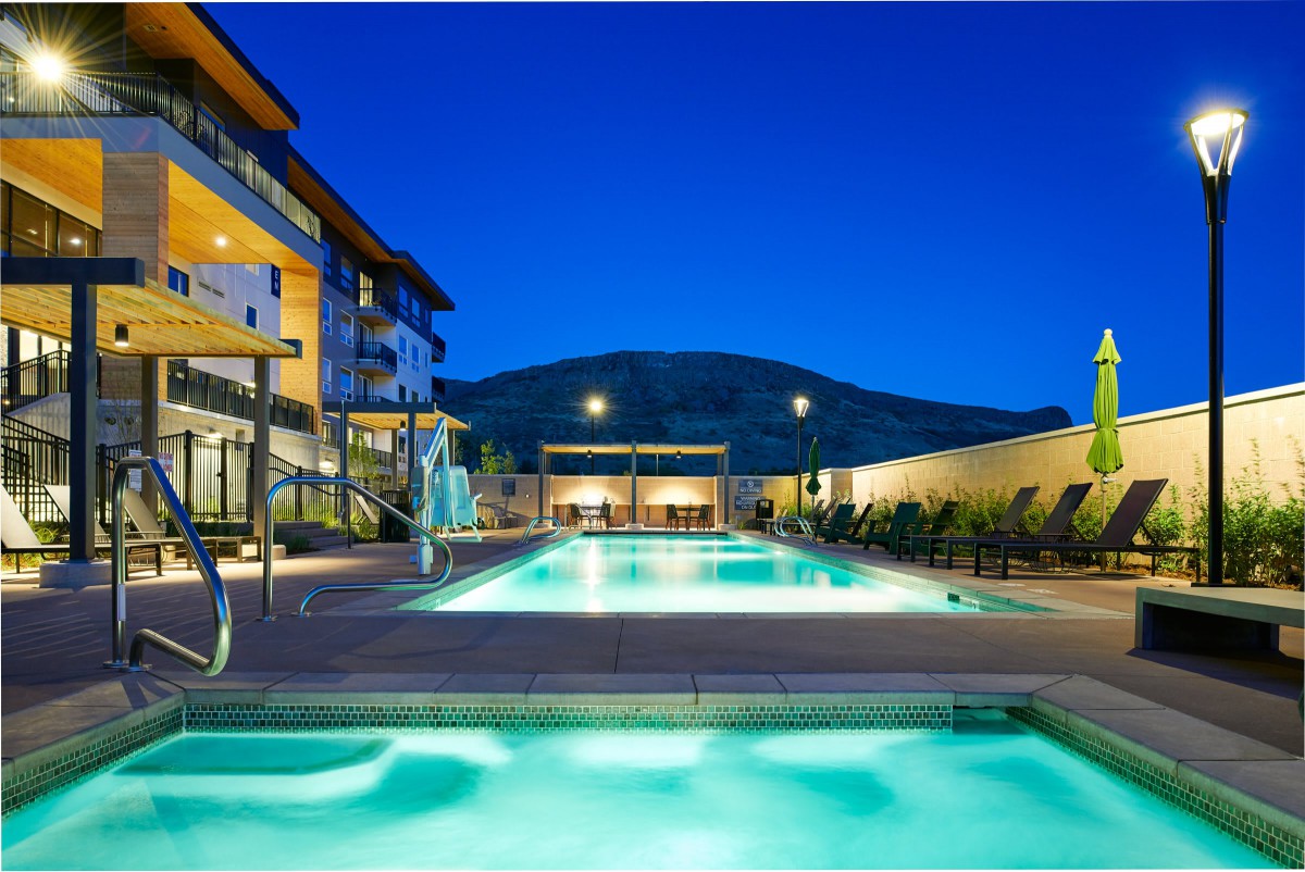 A luxurious outdoor swimming pool at a hotel in the evening, surrounded by modern architecture and scenic views.