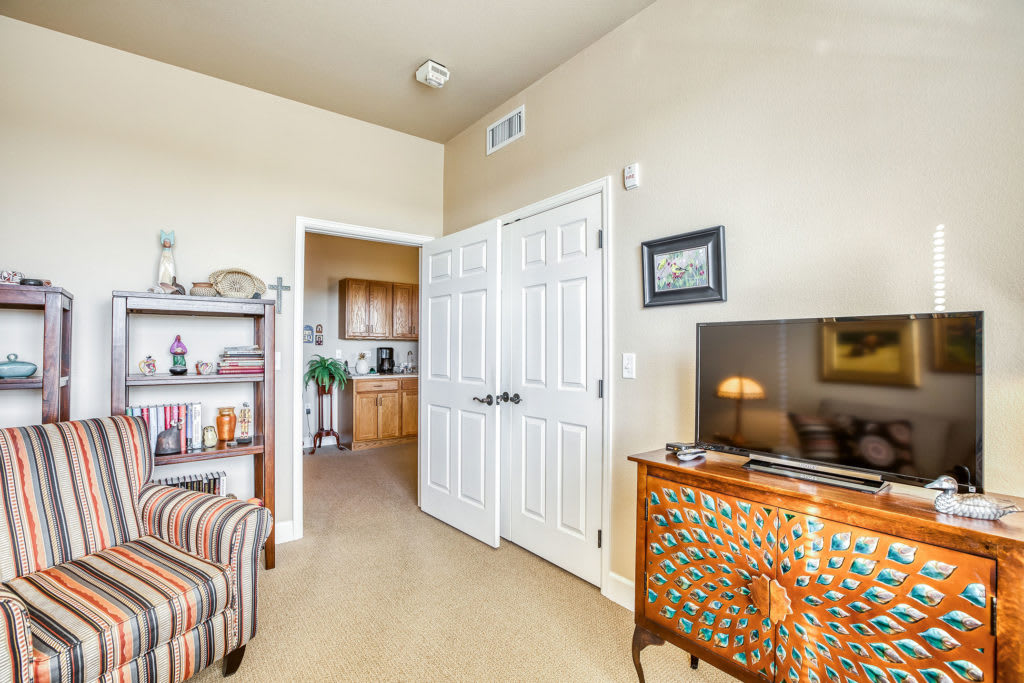 A cozy living room with a television on a decorative cabinet, bookshelf, and a partially open door leading to another room.