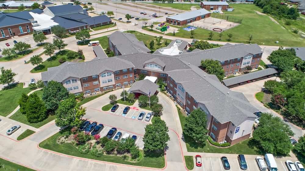 An aerial view of a large residential building complex with surrounding greenery and a parking lot.