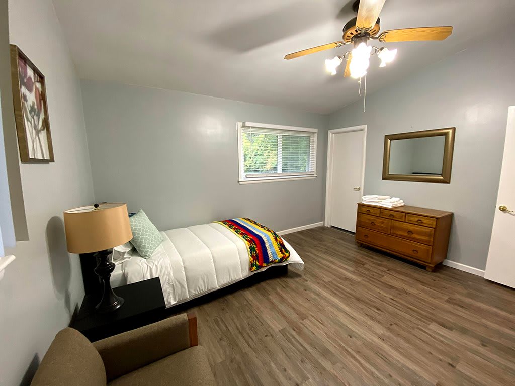 A minimalist bedroom with a single bed, wooden flooring, and modern furniture.