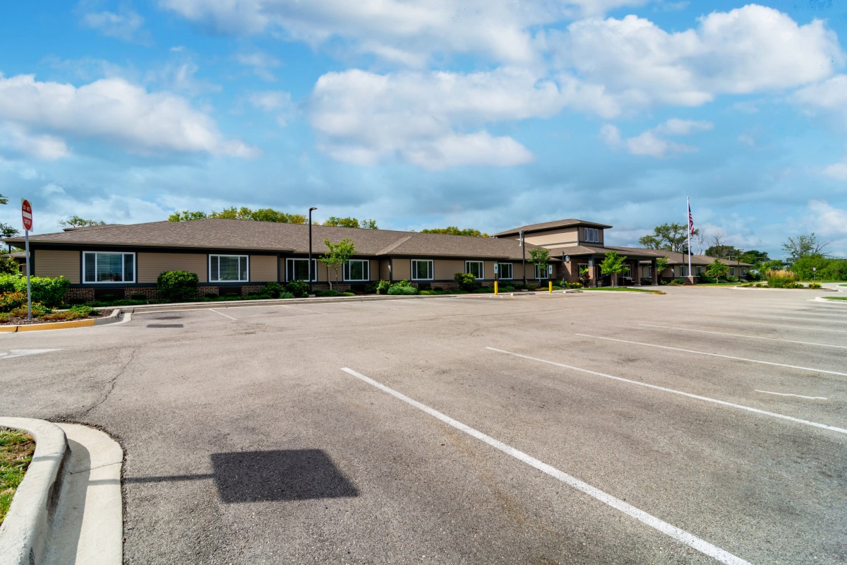 An empty parking lot in front of a low, elongated building under a partly cloudy sky.
