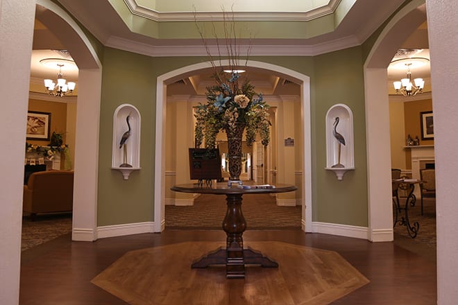 A beautifully decorated foyer featuring a central table with floral arrangements, flanked by artwork in a sophisticated setting.