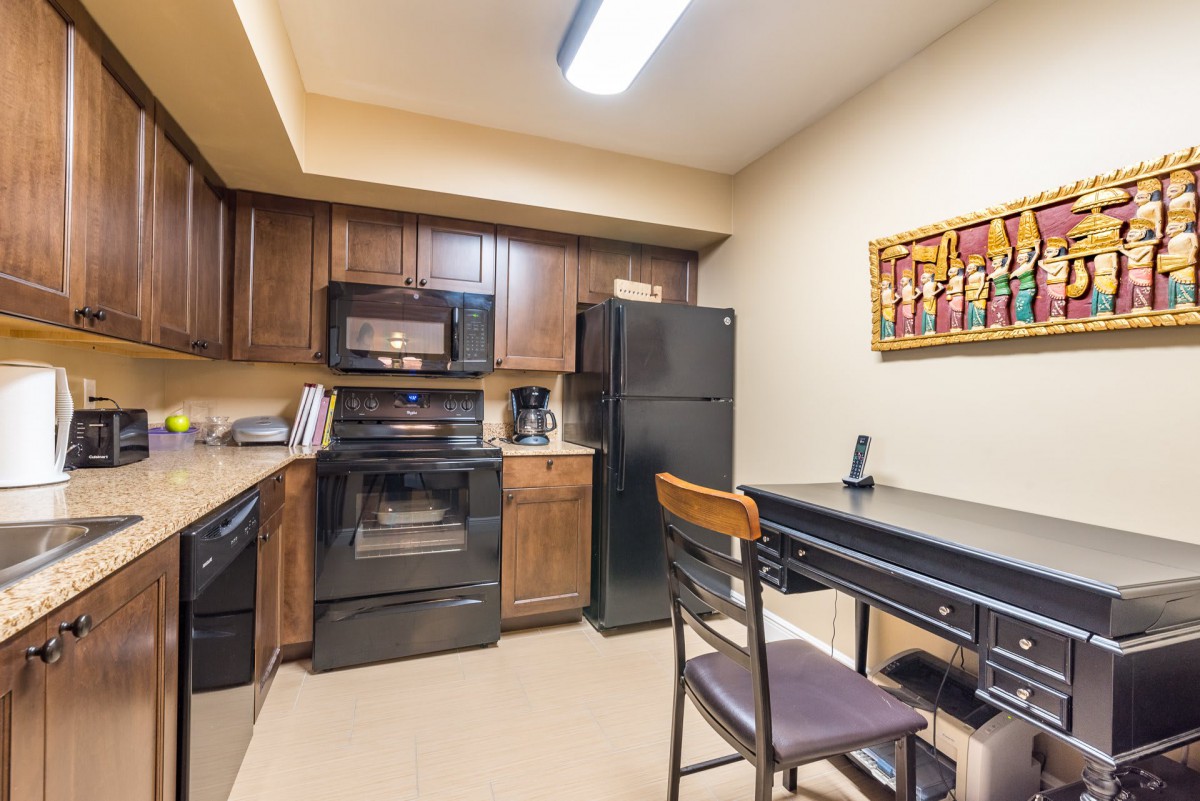 A cozy kitchen with dark wooden cabinets and black appliances, featuring a small dining table and colorful artwork on the wall.