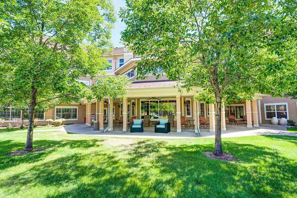 A beautiful residential building surrounded by lush green trees and a well-maintained lawn on a sunny day.