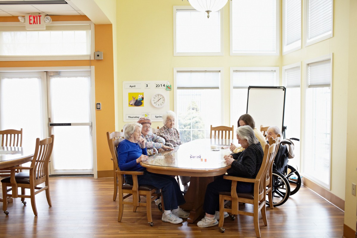 Elderly individuals sitting together in a nursing home, engaging in social activities at a table.