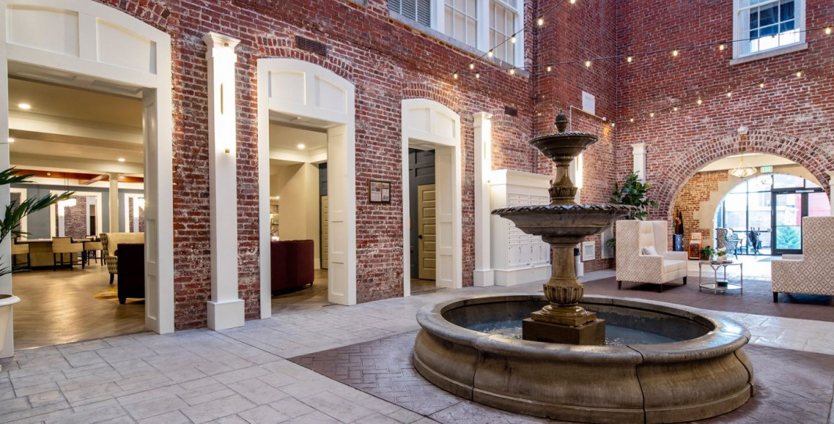A quaint courtyard featuring a central fountain, surrounded by red brick walls and illuminated by string lights.