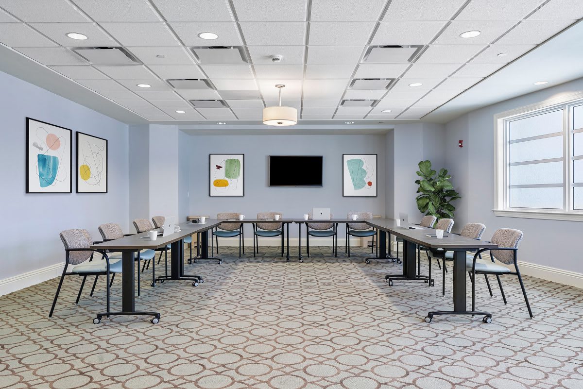 A modern conference room with arranged tables and chairs, featuring a television and decorative art on the walls.