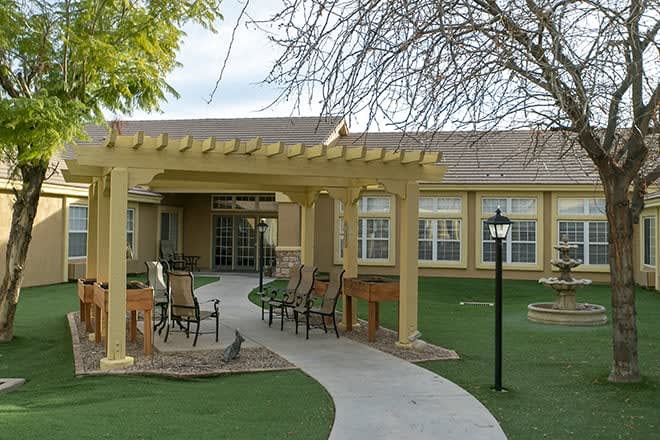 A cozy outdoor patio area with a pergola and seating, surrounded by well-maintained landscaping in front of a building.