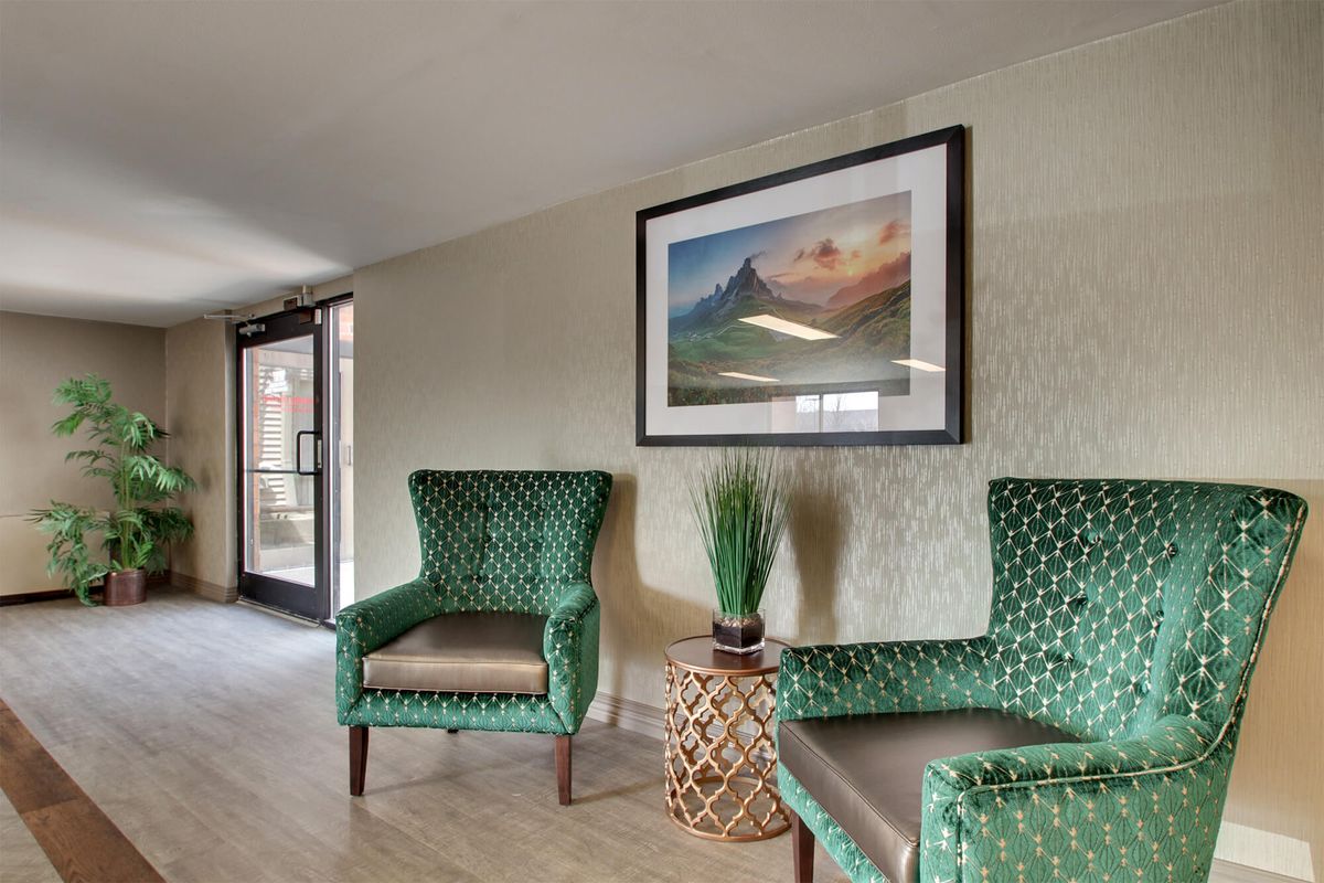 A cozy seating area with two green armchairs, a small table with a plant, and a framed landscape artwork on the wall.
