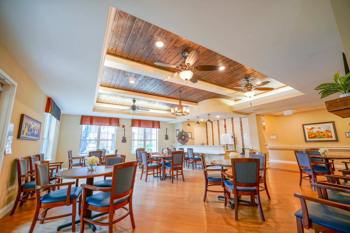 A spacious dining area with ceiling fans and wooden floors, featuring neatly arranged tables and chairs.