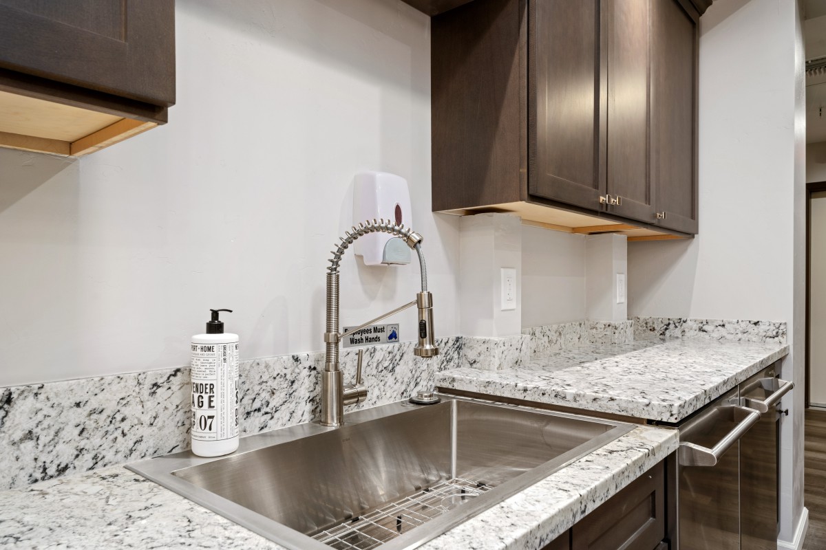 A modern kitchen sink with a marble countertop and a sleek faucet, accompanied by a soap dispenser.