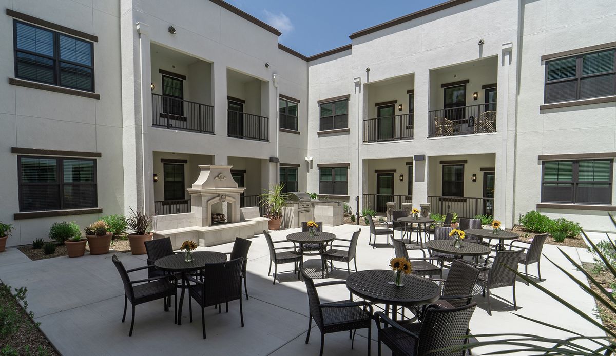 An outdoor courtyard with tables, chairs, and a central fireplace surrounded by a two-story building.