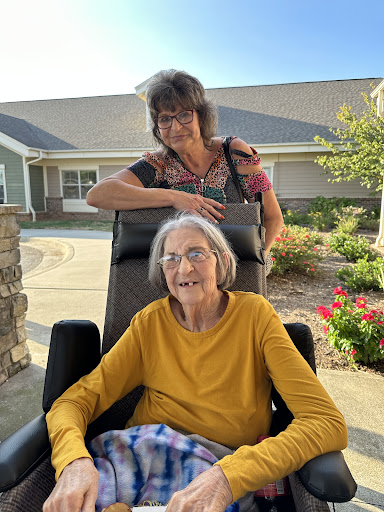 A warm moment shared between a caregiver and an elderly woman enjoying a sunny day outside.