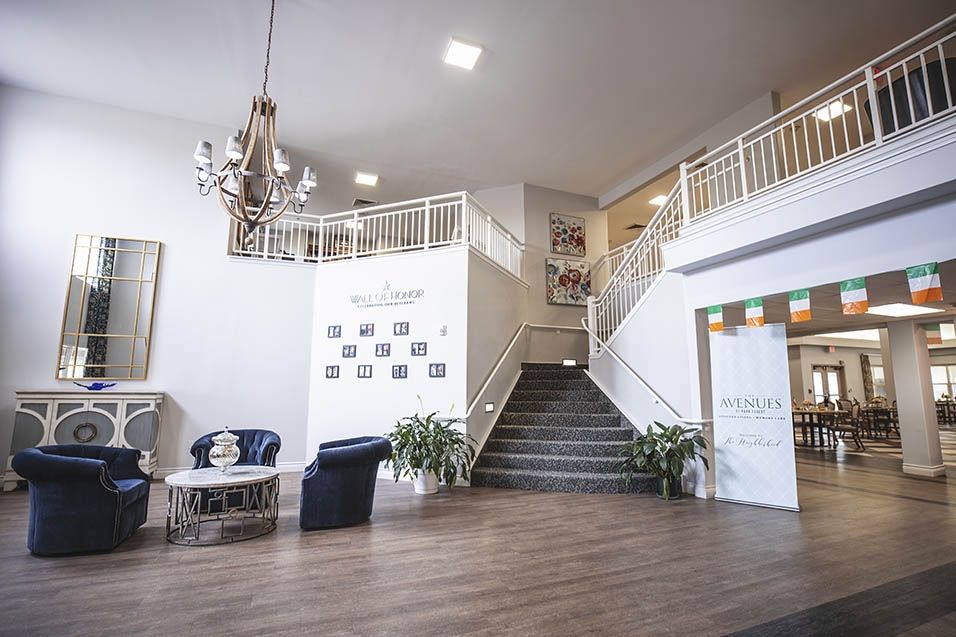 A spacious lobby interior featuring a central staircase, elegant chandelier, and seating area with plants.