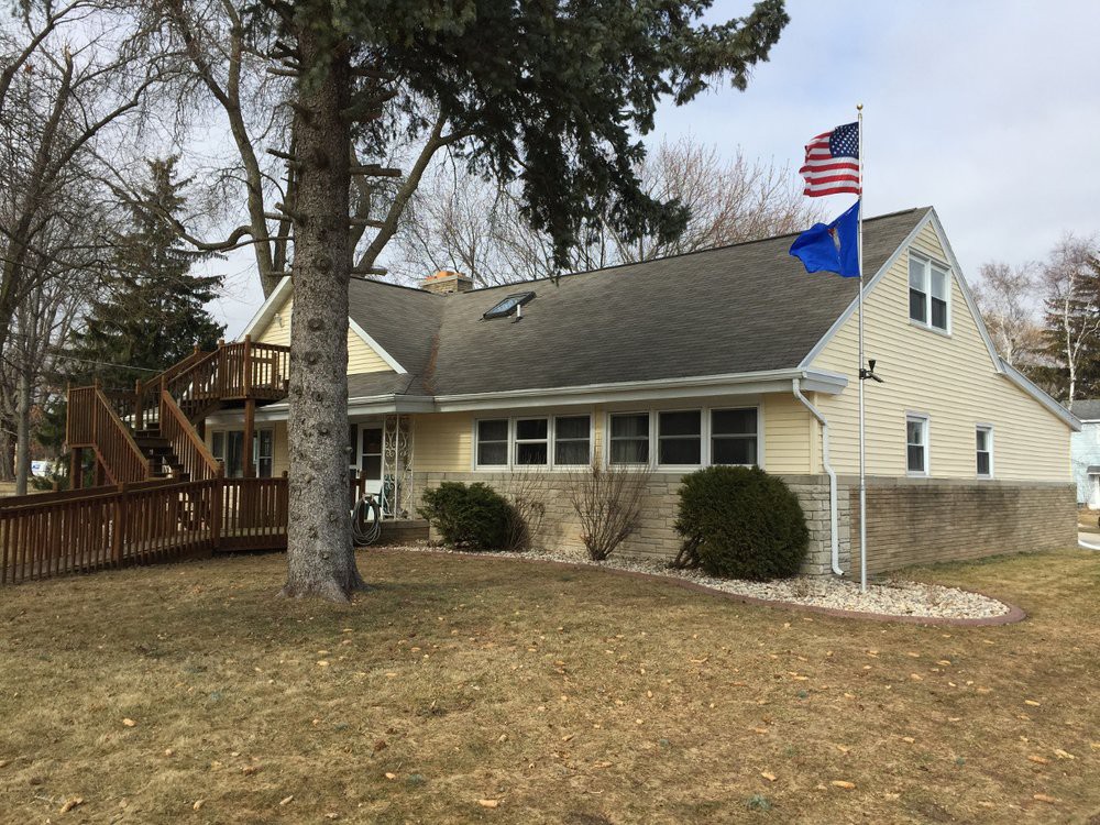 A residential house with a well-kept yard, featuring two flags on the roof and surrounded by trees.