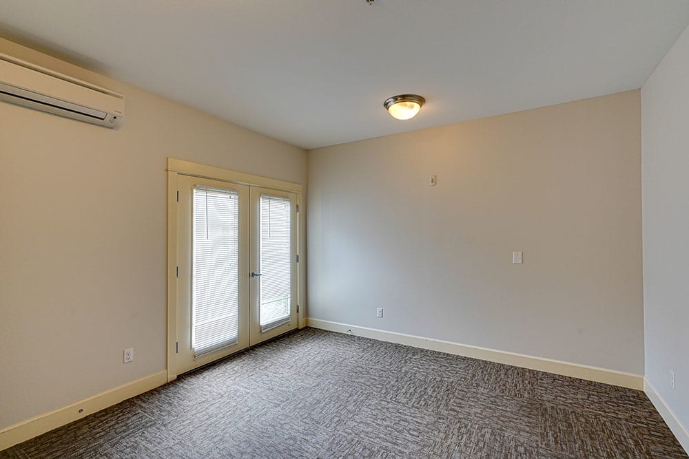 An empty room with carpet flooring, featuring double doors and a ceiling light.
